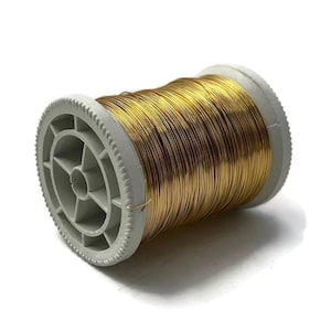 May include: A spool of gold-colored wire. The wire is tightly wound around a gray plastic spool. The spool has a circular design with a series of holes and a ridged edge. The wire appears to be made of a shiny metal.