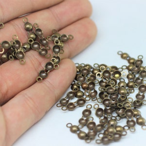 Peut inclure: Un tas de perles en métal de couleur or antique avec deux boucles sur chaque perle. Les perles sont rondes et ont un dessus bombé.