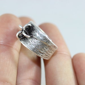 May include: A silver ring with a textured band and a decorative design on the top.