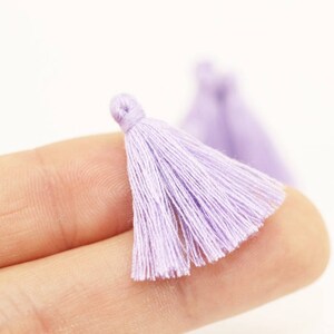 Puede incluir: Un primer plano de una pequeña borla de color lila claro. La borla está hecha de hilos suaves y finos y mide aproximadamente 2,5 cm de largo.