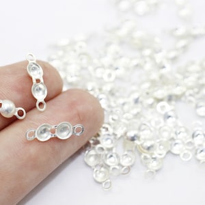 Peut inclure: Des embouts de perles en métal argenté avec deux boucles à chaque extrémité. Les embouts de perles sont disposés en ligne sur un doigt.