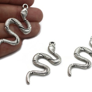 Könnte beinhalten: Drei silberne Schlangenanhänger mit strukturierter Oberfläche. Die Schlangenanhänger sind in einer gekrümmten Position mit einer Öse oben zum Anbringen an einer Halskette oder einem Armband.