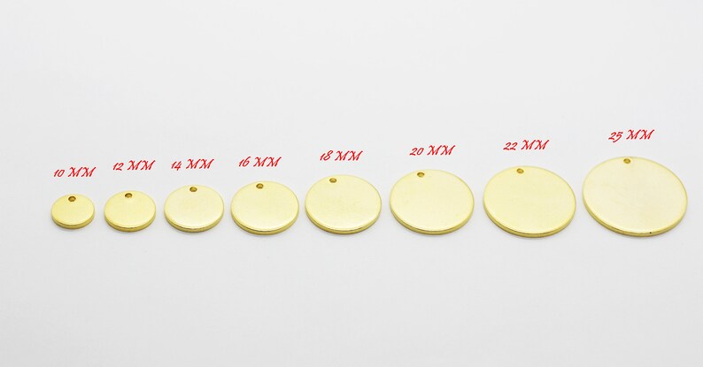 May include: A collection of gold-colored, round metal blanks in various sizes, ranging from 10 mm to 25 mm. Each blank has a small hole at the top for attaching to jewelry or other crafts. The sizes are labeled in red text.