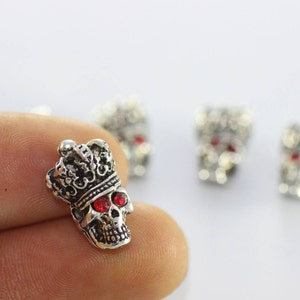 May include: Silver skull charm featuring a crown and red rhinestone eyes. The skull is intricately carved and is a popular choice for jewellery making.