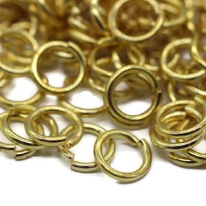 May include: A pile of gold jump rings, a type of metal ring used in jewelry making.