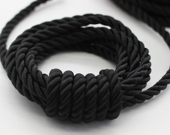 May include: Black braided cord, a thick, twisted rope made of fabric. The cord is coiled into a circle and tied in a knot.