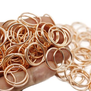 May include: A large pile of rose gold jump rings. The rings are all the same size and are arranged in a random pattern.