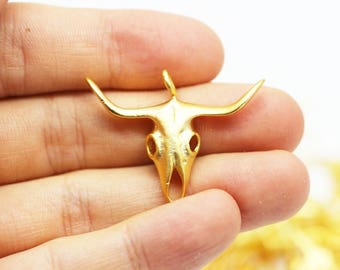 May include: Gold-toned metal bull skull pendant charm. The pendant is detailed with a textured surface and features a loop at the top for attaching to a chain or cord.