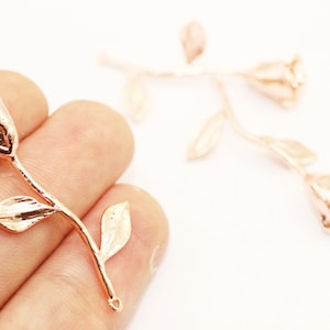 May include: Rose gold rose stem charms with a delicate design. The charms feature a rose bud with leaves and a loop for attaching to jewelry.
