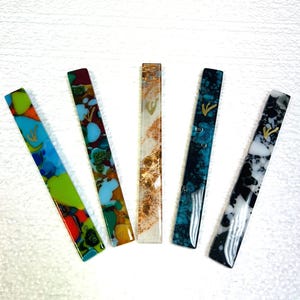 May include: Five colorful glass mezuzahs with a gold Hebrew letter Shin on each. The mezuzahs are in various patterns, including blue, green, red, white, and black.