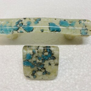 May include: Two glass cabinet knobs with a white and blue speckled design. The larger knob is a pull handle, and the smaller knob is a square.
