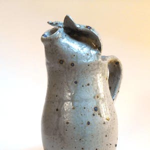 May include: A light grey ceramic jug with a distinctive spout and handle. The jug has a speckled glaze with brown and blue accents.