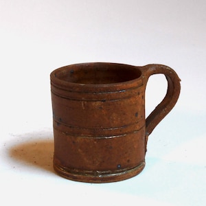May include: A brown ceramic mug with a rounded handle. The mug has a rustic, handmade look with a speckled glaze.