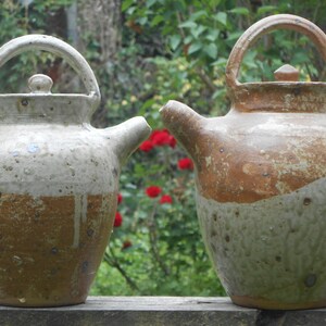 May include: Two ceramic teapots with brown and white glaze. The teapots have a rounded body and a spout on the side. The teapots are sitting on a wooden surface.