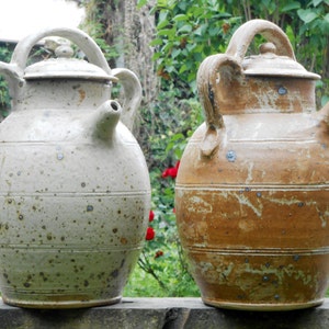 Op de afbeelding: Twee keramische kannen met deksels en handvatten. De kan links is wit met bruine vlekken. De kan rechts is bruin met witte vlekken.