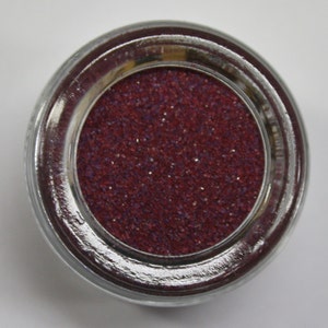 May include: A small round jar filled with a deep red glitter. The glitter is fine and has a slight shimmer.