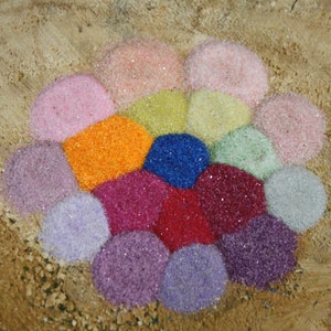 May include: A colorful arrangement of small, sparkly, round beads in various shades of pink, orange, yellow, green, blue, purple, and red. The beads are arranged in a circular pattern on a brown, textured surface.