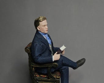 May include: A miniature figurine of a person with light brown hair, wearing a dark blue pinstriped suit, a light blue cravat, and dark shoes. The figure is seated in a dark, ornate wooden chair with patterned upholstery, holding a small book.
