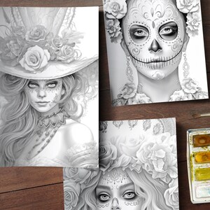 May include: Three black and white coloring book pages featuring detailed illustrations of women with floral headpieces and sugar skull makeup. The pages are on a wooden surface with a watercolor paint set.