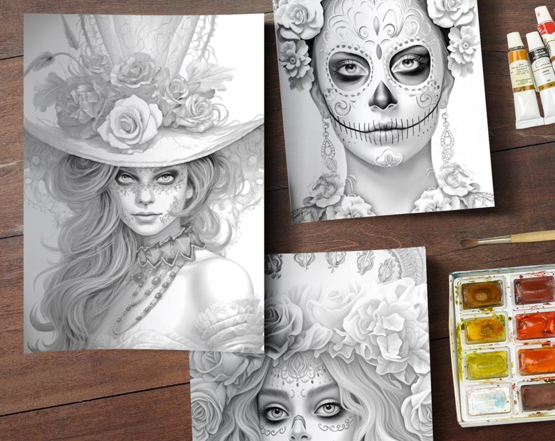 May include: Three black and white coloring book pages featuring detailed illustrations of women with floral headpieces and sugar skull makeup. The pages are on a wooden surface with a watercolor paint set.