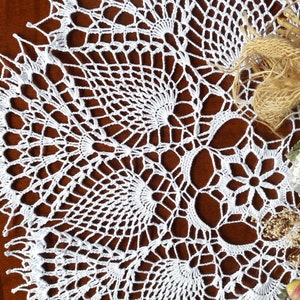 May include: White crocheted doily with a delicate floral pattern. The doily is circular and has a scalloped edge.