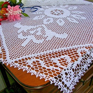 May include: White crocheted tablecloth with a delicate floral pattern. The tablecloth is laid on a wooden table.
