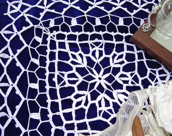 May include: White crocheted lace tablecloth with a geometric pattern on a dark blue background.