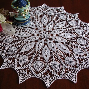 May include: White crocheted doily with a delicate, intricate design. The doily has a circular shape with a central motif and radiating patterns.