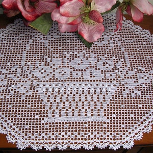 May include: White crocheted doily with a delicate floral pattern. The doily is laid on a wooden surface.