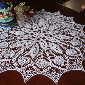 May include: White crocheted doily with a delicate, intricate design. The doily is circular with a scalloped edge and features a central motif of a starburst.