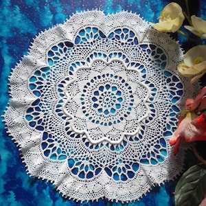 May include: White crocheted doily with a delicate floral pattern, against a blue background.