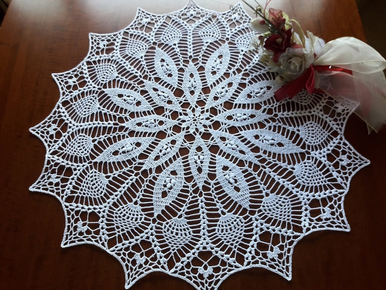 May include: A white crocheted doily with a delicate floral pattern. The doily is circular and has a scalloped edge.