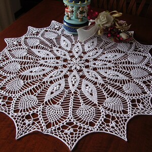 May include: White crocheted doily with a delicate floral pattern. The doily is circular and has a scalloped edge.