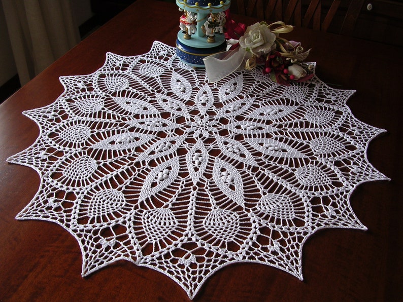 May include: White crocheted doily with a delicate floral pattern. The doily is circular and has a scalloped edge.
