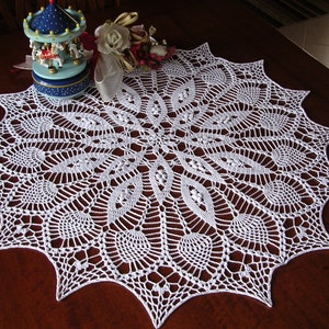 May include: White crocheted doily with a delicate, intricate design. The doily is circular with a scalloped edge and features a repeating pattern of leaves and flowers.
