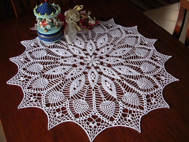 May include: White crocheted doily with a delicate, intricate design. The doily is circular with a scalloped edge and features a repeating pattern of leaves and flowers.