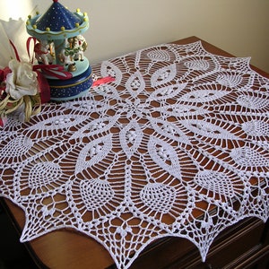 May include: White crocheted table runner with a delicate, intricate design. The runner features a circular pattern with a starburst effect and a scalloped edge.