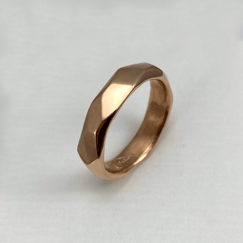 Puede incluir: Un anillo de banda de oro rosa con un dise&ntilde;o facetado y geom&eacute;trico. El anillo est&aacute; hecho de un metal liso y pulido.