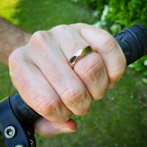 Puede incluir: Una mano con un anillo geom&eacute;trico dorado. El anillo est&aacute; en el dedo medio de la mano. La mano est&aacute; sujetando un manillar negro.