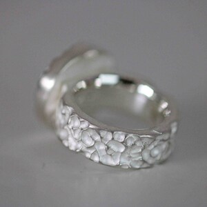 May include: Close-up of a silver ring with a textured band and a smooth, rounded top. The ring's band features a detailed, organic pattern, and the overall design has a handcrafted appearance. The ring is likely made of sterling silver.