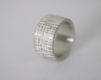 May include: A silver ring with a textured, geometric pattern. The ring is wide and has a polished finish.