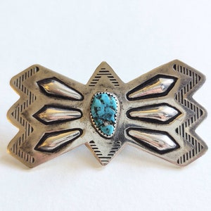 May include: A silver and turquoise Native American style belt buckle with a geometric design.