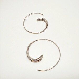 May include: A pair of silver hoop earrings with a unique spiral design. The earrings are made of thin metal and have a smooth finish.