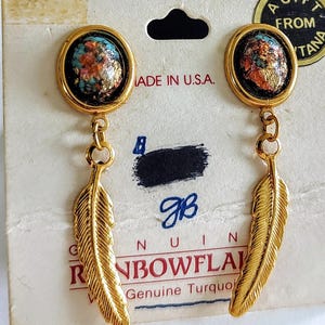 May include: Gold-toned earrings with a turquoise and gold-flecked oval top and a dangling feather design. The earrings are attached to a white card with the text "MADE IN U.S.A." and "RAINBOWFLA".