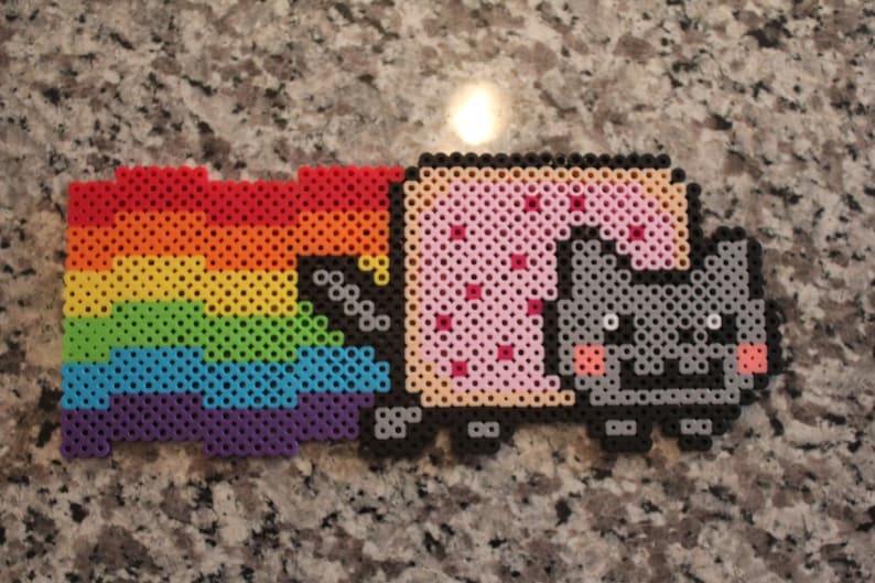 Pu&ograve; includere: Un design pixel art di Nyan Cat, un gatto con un corpo Pop-Tart, che vola nello spazio con una scia arcobaleno. Il gatto &egrave; grigio con guance rosa e il Pop-Tart &egrave; rosa con spruzzi rossi. L'arcobaleno &egrave; fatto di perline rosse, arancioni, gialle, verdi, blu e viola.