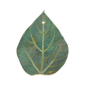 Puede incluir: Un colgante o adorno con forma de hoja que presenta un acabado de pátina en verde oscuro y azul verdoso con vetas doradas metálicas visibles. El objeto tiene una punta afilada, una base redondeada y un pequeño orificio circular para colgar.
