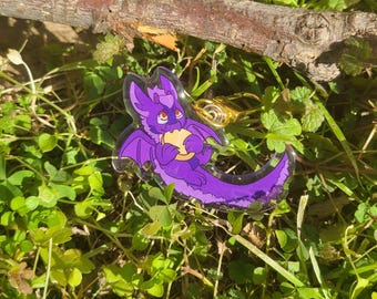 May include: Purple dragon keychain with a gold chain and a small yellow object in its claws.