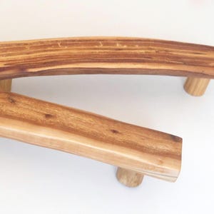 Può includere: Due maniglie per mobili in legno dal design naturale e curvo. Le maniglie sono realizzate in legno marrone chiaro con venature visibili e sono montate su piccoli perni cilindrici in legno. L'estetica generale è rustica e organica.