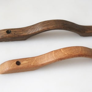 May include: Two wooden cabinet door handles with a curved design. The handle on the top is dark brown and the handle on the bottom is light brown.