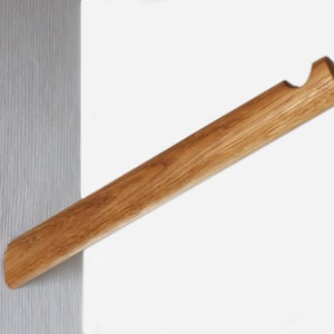 Könnte beinhalten: Ein Wand-Kleiderbügel aus Holz mit einem einfachen Design. Der Kleiderbügel ist aus Naturholz gefertigt und hat eine leicht geschwungene Form.